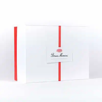Un coffret avec un couvercle blanc divisé en son milieu par un ruban rouge. Le logo "Belle-Maman" est collé sur ce couvercle.